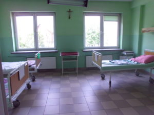 Kilkuosobowa sala chorych przed remontem w Oddziale w budynku Szpitala przy Plac Kuźnice 1 - zielone ściany, ciemne płytki na posadzkach.